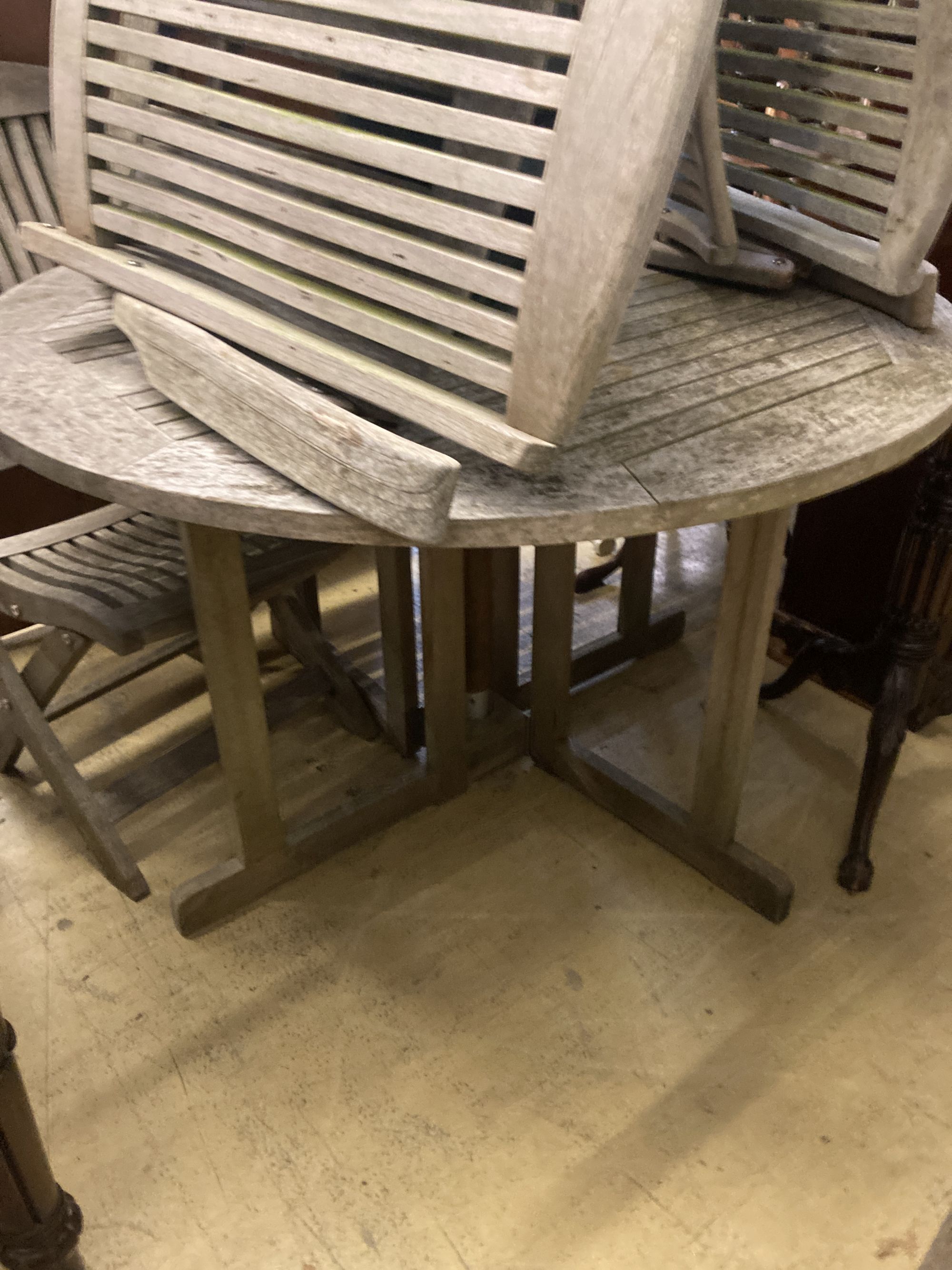 A circular weathered teak garden table, diameter 120cm, together with a garden parasol and four folding garden chairs (two with arms)